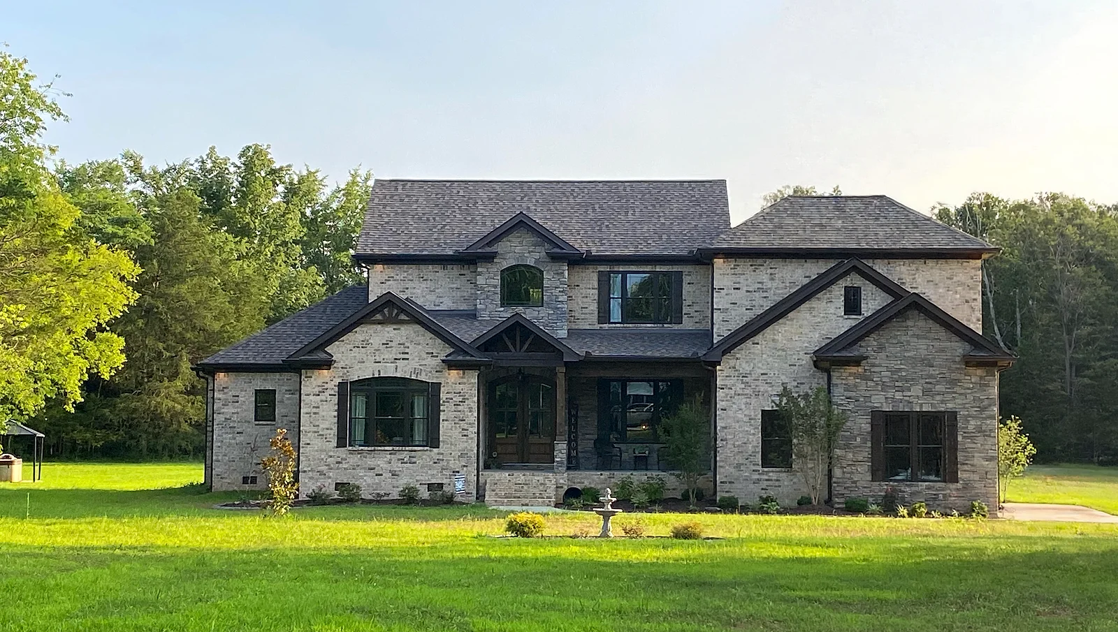 A completed custom home in Middle Tennessee: stone and brick elevation with gabled dormers, timber porch brackets, and a newly sodded lawn.